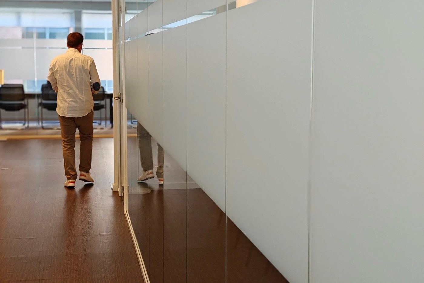 Een medewerker loopt door een glazen gang, op weg naar binnen